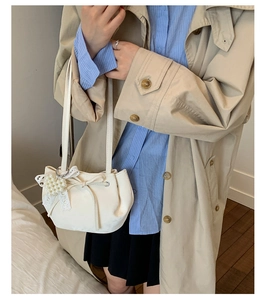 Detail of cream white shoulder bag with lace bow, pearl pendant and drawstring pleats