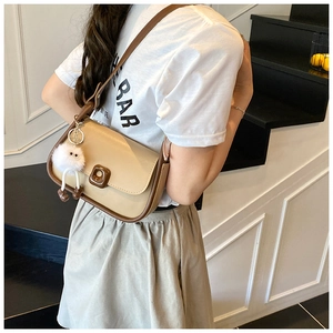 Crossbody view of a vintage beige and dark coffee shoulder bag with a white plush charm