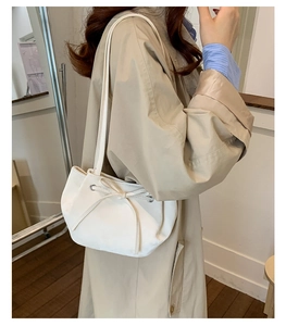 Detail view of white drawstring bucket bag with bow on beige coat shoulder