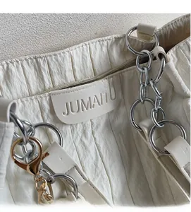 Dettaglio borsa tote in tela crema plissettata con catena argento e logo inciso