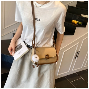 Close-up of a tan crossbody bag with a brown square clasp and white plush monster charm