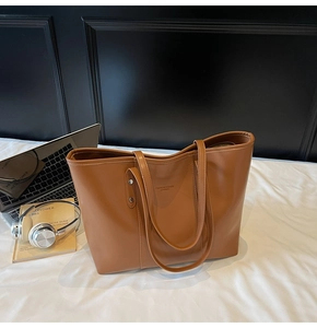 Detailweergave van bruine PU-leren shopper op wit bed met laptop en koptelefoon