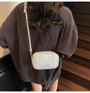 Gros plan d'un sac bandoulière en cuir blanc avec grain litchi porté par un mannequin