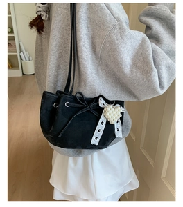 Detail of black suede bucket bag featuring a white pearl heart charm and lace ribbon bow