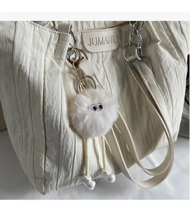Dettaglio di un ciondolo a forma di mostro peloso beige su una grande borsa tote di tela