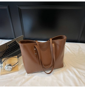 Gedetailleerd zijaanzicht van een grote bruine leren tote bag op een bed met accessoires