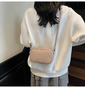 Détail du sac bandoulière beige montrant la texture grainée et les ferrures argentées