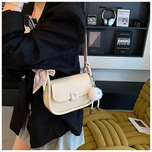 Detail of cream saddle bag featuring a decorative striped silk scarf and plush charm