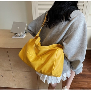 Detail view of large yellow PU leather tote bag with love 15°C embossed text on model shoulder