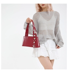 Red leather underarm bag with silver rivet details shown on model with white skirt