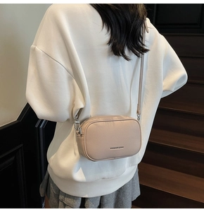 Detail view of beige lychee texture leather crossbody bag shown on a female model