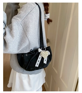 Detail of black velvet shoulder bag with bow drawstring and heart pearl charm accessory