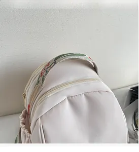 Dettaglio dello zaino in nylon bianco crema con tracolla ricamata e logo in metallo