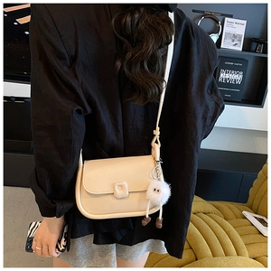 Close-up of cream crossbody bag with plush monster charm on modern interior background