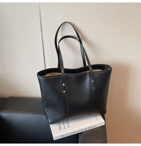 Detail van een zwarte leren shopper met zilveren klinknagels en rits op een bank