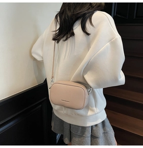 Détail du sac bandoulière minimaliste en cuir beige porté par un mannequin