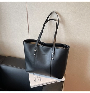 Detail van zwarte PU-lederen tote bag met reliëflogo en metalen noppen aan de zijkant van de tas