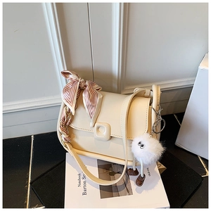 Detail of beige crossbody bag with decorative striped silk scarf and fluffy doll pendant