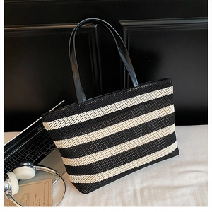 Primer plano de un bolso tote tejido en blanco y negro con asas de cuero y accesorios