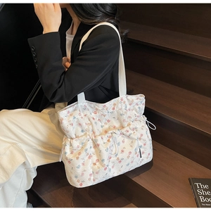 Detail of white floral tote bag with pleated fabric and drawstring on model's shoulder