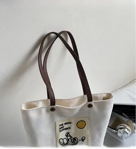 Detail of canvas tote bag featuring brown leather straps and artistic illustration patch
