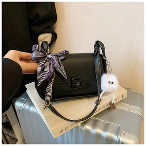 Detail of a premium black leather crossbody bag with striped scarf and plush charm accessory