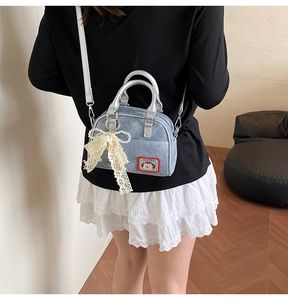 Détail d'un sac à main en denim avec poignées argentées et pendentif nœud en dentelle