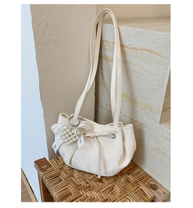 Close-up of cream shoulder bag featuring pleated design and pearl heart lace charm