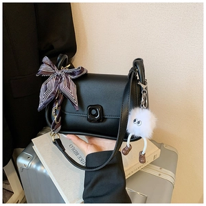 Detail of black leather shoulder bag with striped ribbon and white fuzzy monster charm