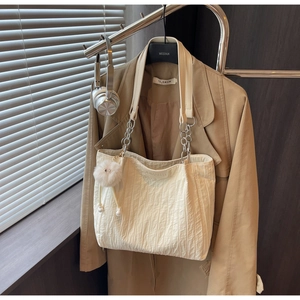 Dettaglio borsa tote in tela beige con etichetta in pelle e tracolla a catena metallica