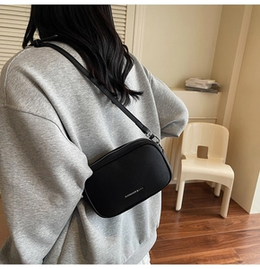 Détail d'un sac bandoulière noir en cuir grainé avec logo argenté et bandoulière
