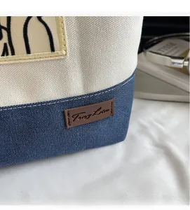 Detail of the high-quality canvas stitching and leather logo on a beige and navy tote bag