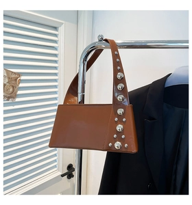 Detail shot of brown glossy leather bag featuring silver metal rivets and a slim handle