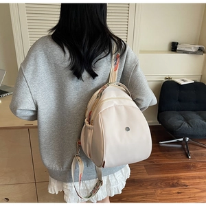 Dettaglio zaino in nylon crema con tracolla ricamata colorata e tasche multiple