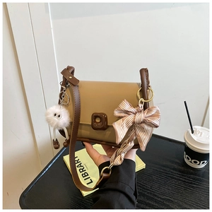 Detail of khaki PU leather crossbody bag with brown trim and plush monster charm
