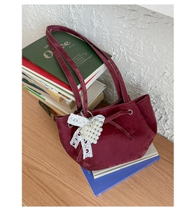 Detail of burgundy velvet handbag featuring lace bow and pearl charm on books