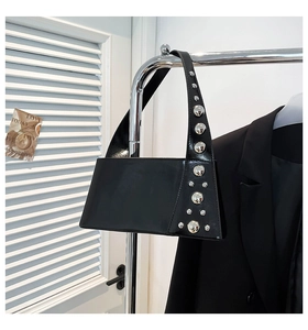 Close-up of black glossy shoulder bag with silver spherical studs and asymmetric shape