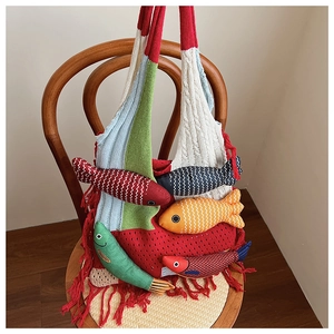 Detail of color-block knit tote bag with 3D fish charms and vibrant red fringe hanging on chair