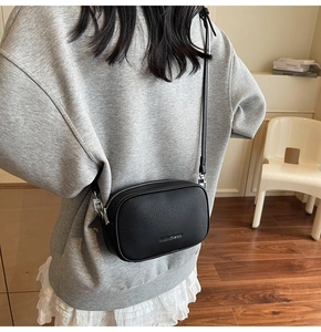 Détail du sac bandoulière en cuir grainé noir avec logo argenté porté par un mannequin