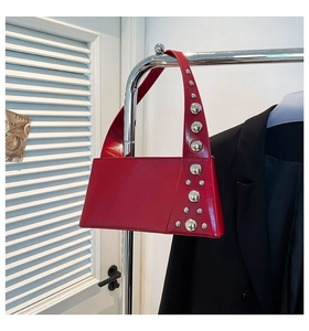 Detailed view of red glossy leather shoulder bag with silver rivet studs and sleek texture