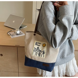 Close-up of beige and navy canvas tote bag with contrast stitching and leather strap details