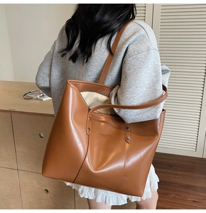 Detail van grote bruine tote bag met metalen klinknagels en modetekst over de schouder