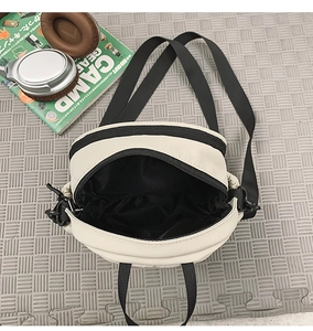 Detail view of cream small crossbody bag showing open zipper and black inner storage space