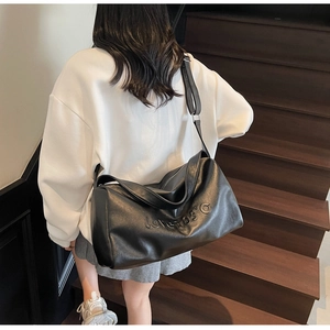 Close-up of black tote bag with Love 105 embossed text worn by a model on stairs