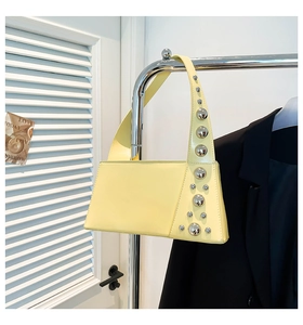 Close-up of a lemon yellow baguette bag with polished silver rivets on a chrome hanger