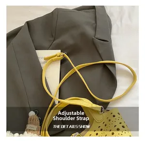 Détail de la bandoulière réglable et du motif ajouré sur ce sac seau jaune porté en travers