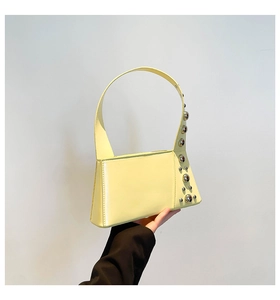 Detail of light yellow patent leather shoulder bag with decorative silver metal studs