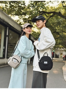 Outdoor lifestyle view of two models carrying casual nylon crossbody bags in grey and black