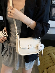 Elegant off-white faux leather saddle bag with plush charm shown on a model's shoulder