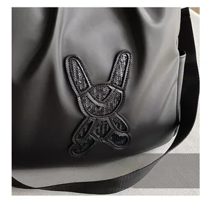 Detail of a black leather backpack with a shiny sequined rabbit patch and woven strap